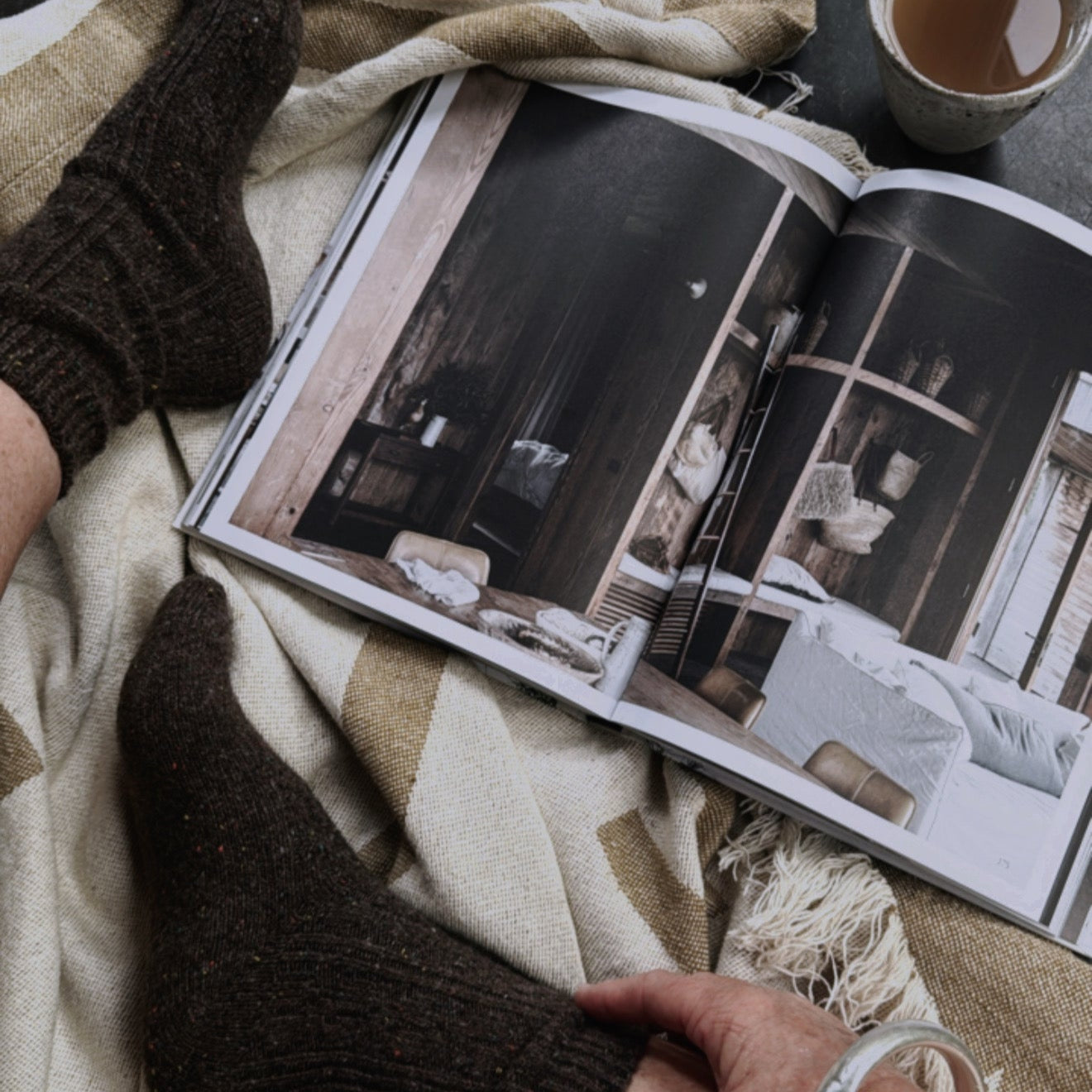Person reading a magazine with feet up on a blanket, wearing socks.