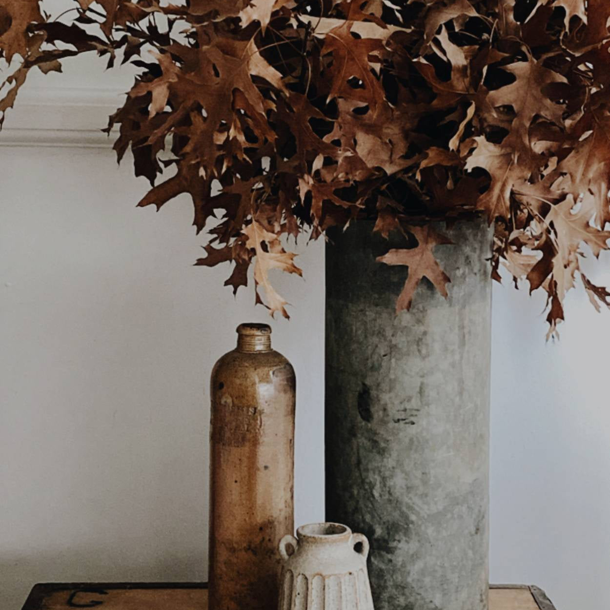 Decorative arrangement with dried leaves, vases, and a textured surface.