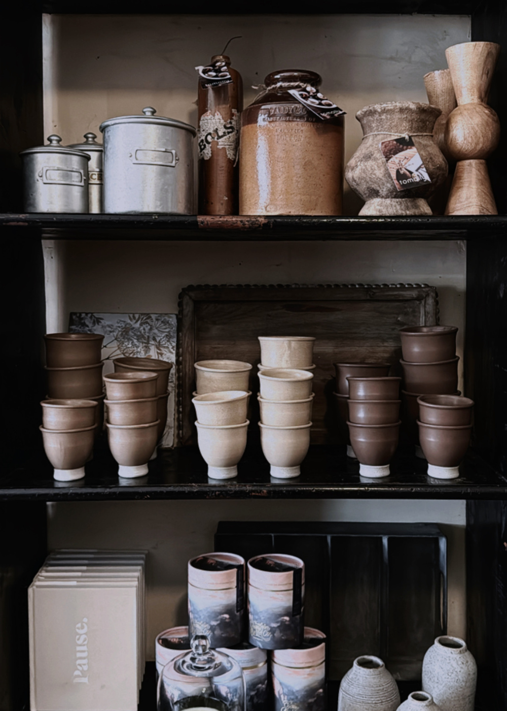 A shelf filled with various handmade pottery items, including cups and vases, with a soft matte finish in beige, brown, and gray colors.