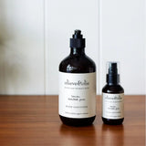 Two amber pump bottles of Olieve & Olie Lemon Scented Gum Hand Sanitizer in 500ml and 100ml sizes on a wooden surface.